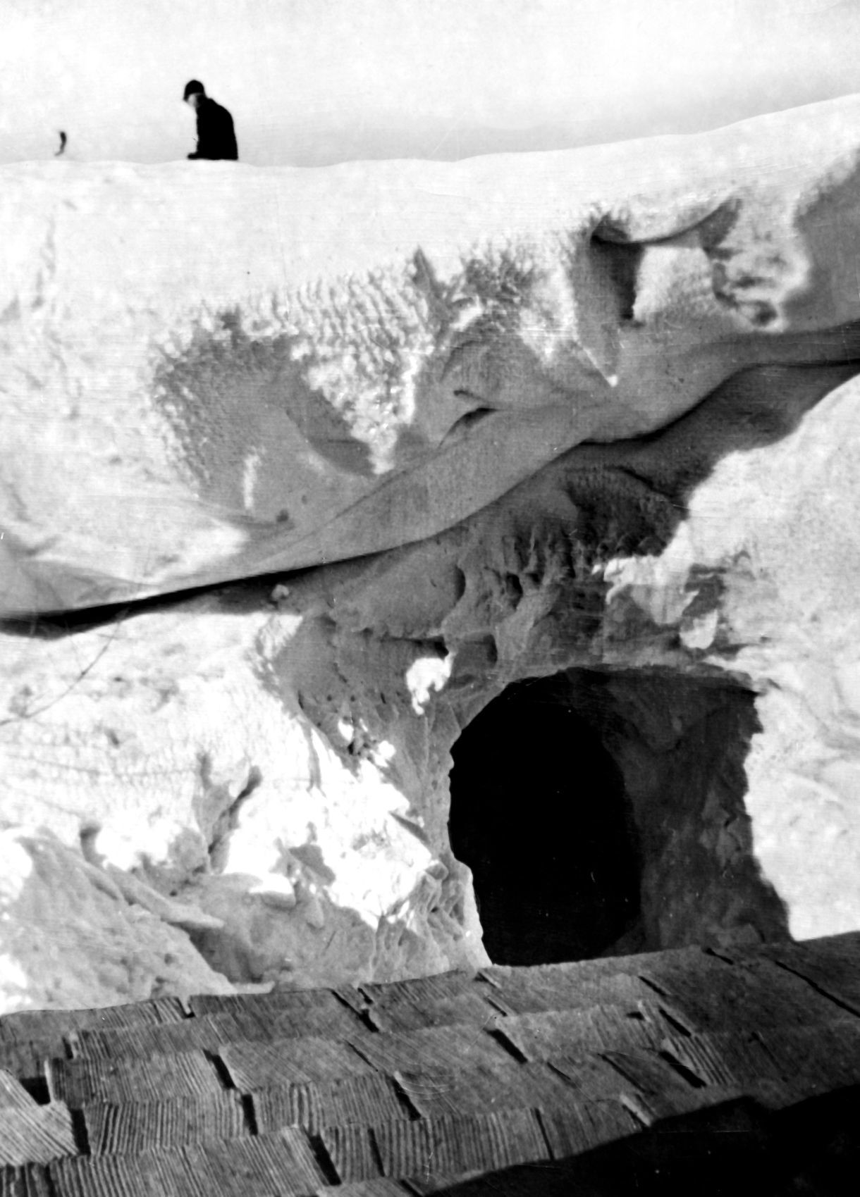 The E.F. Goransen farm, 8 miles west of Gurley, Neb. Miss Marie Goranson took the photo from the roof of the corncrib (shingles shown in foreground.) The hole dug in the drift is several feet above the ground and leads to the window of another building where coal is stored. Mr. Goranson is standing on the top of a brooder house. Only a pipe remains above the snow. Published Jan. 25, 1949.